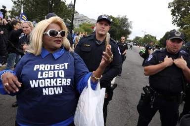 An LGBTQ activist takes a selfie with police in the street outside the U.S. Supreme Court as it hears arguments in a major LGBT rights case in Washington