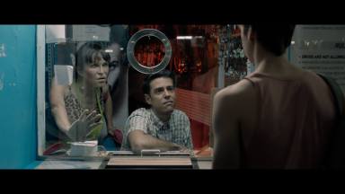 Three people stand at a booth in a scene of “Phantom of the Sauna”
