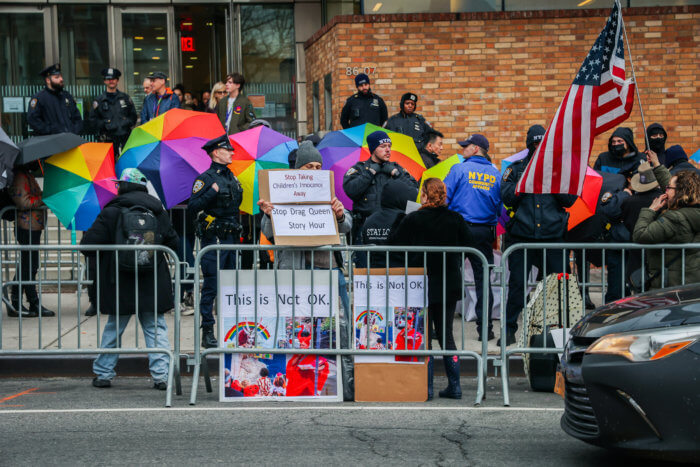 Opponents of Drag Story Hour hold signs near the barricade.