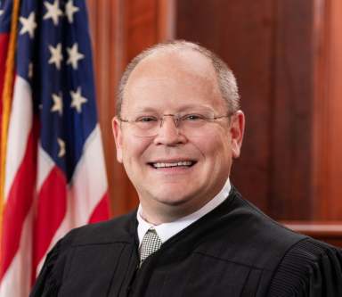 Circuit Judge Toby Heytens next to an American Flag.