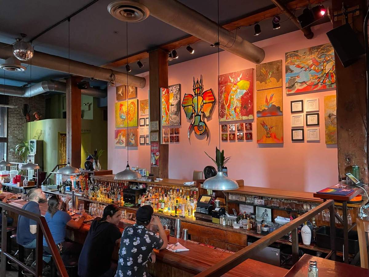 Patrons discuss Craig Anthony Miller’s (aka CAM) artwork on the wall from their bar stool at Superfine’s sunken bar in September 2022.