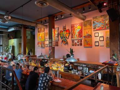 Patrons discuss Craig Anthony Miller’s (aka CAM) artwork on the wall from their bar stool at Superfine’s sunken bar in September 2022.