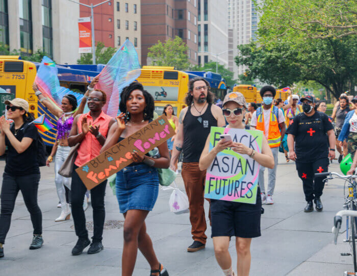 Blasian Pride marchers show their signs as they proceed along the sidewalk.